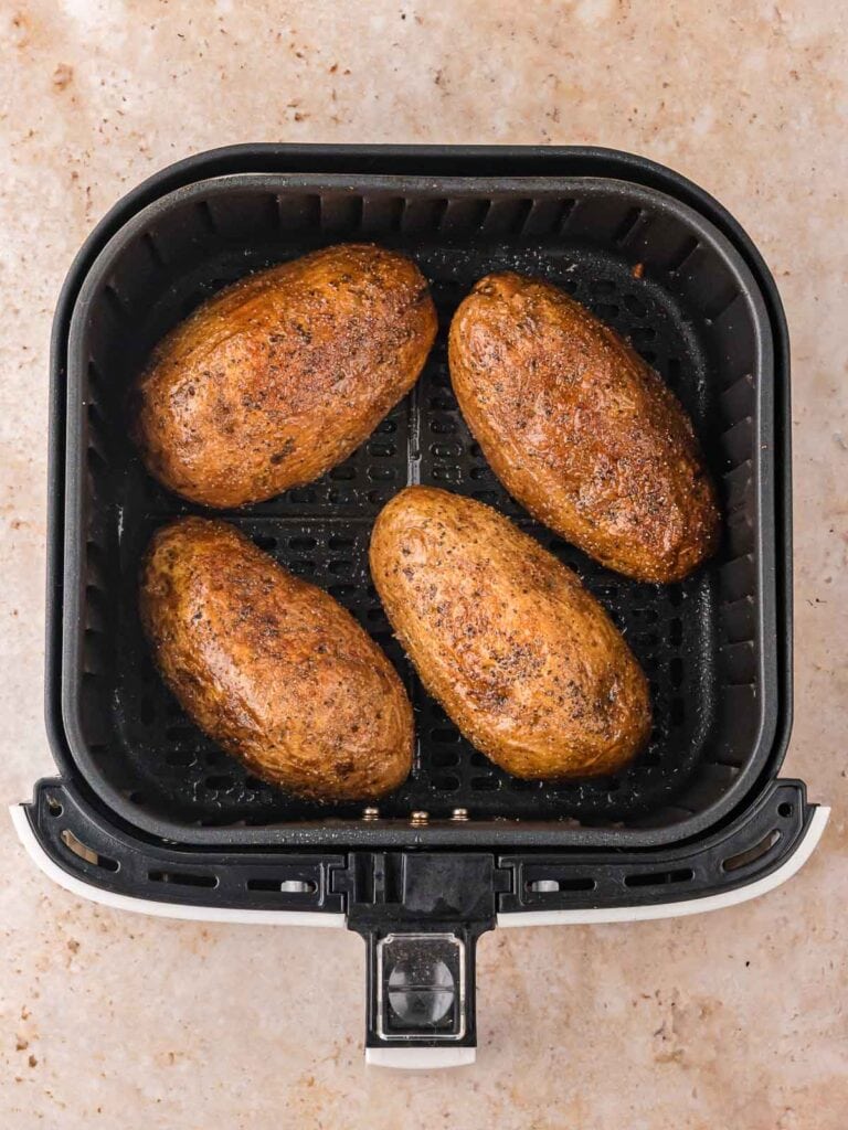 Four seasoned russet potatoes cooking in an air fryer basket.