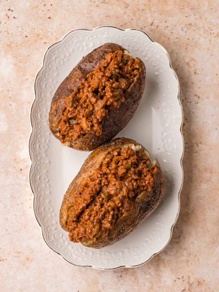 Two baked potatoes topped with sloppy joe mix on a white platter.