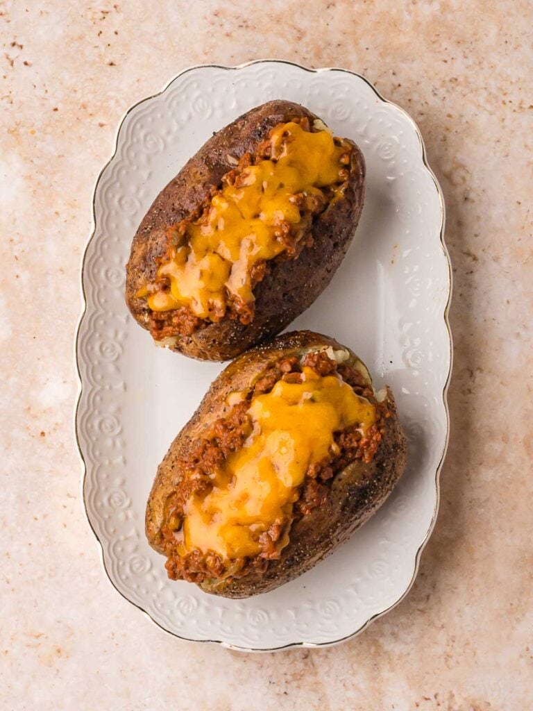Two sloppy joe baked potatoes topped with melted cheddar cheese.
