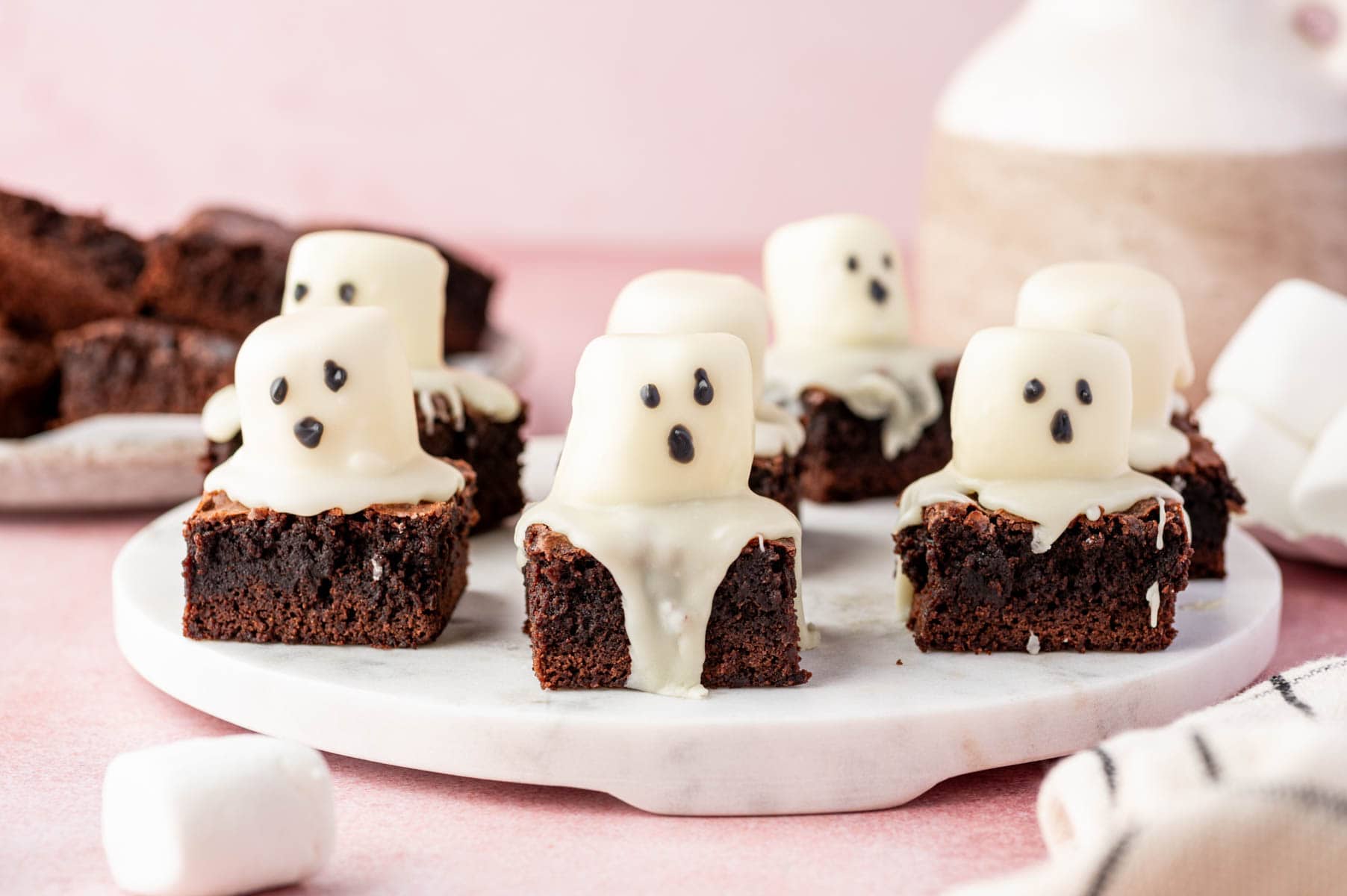 Fudgy chocolate brownies topped with marshmallow ghosts coated in white chocolate and dotted with black icing eyes and mouths for a spooky effect.