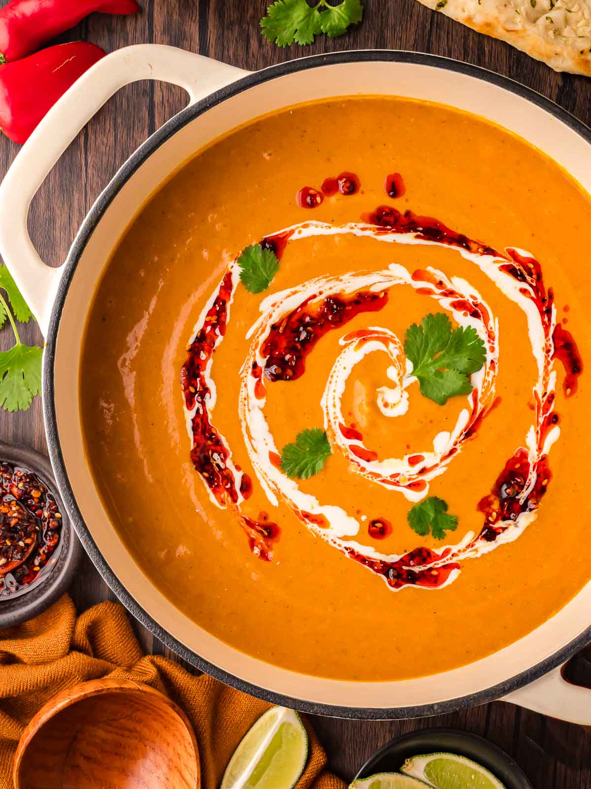 Close-up of pumpkin coconut curry soup with swirled cream, chili oil, and cilantro garnish in a white Dutch oven.
