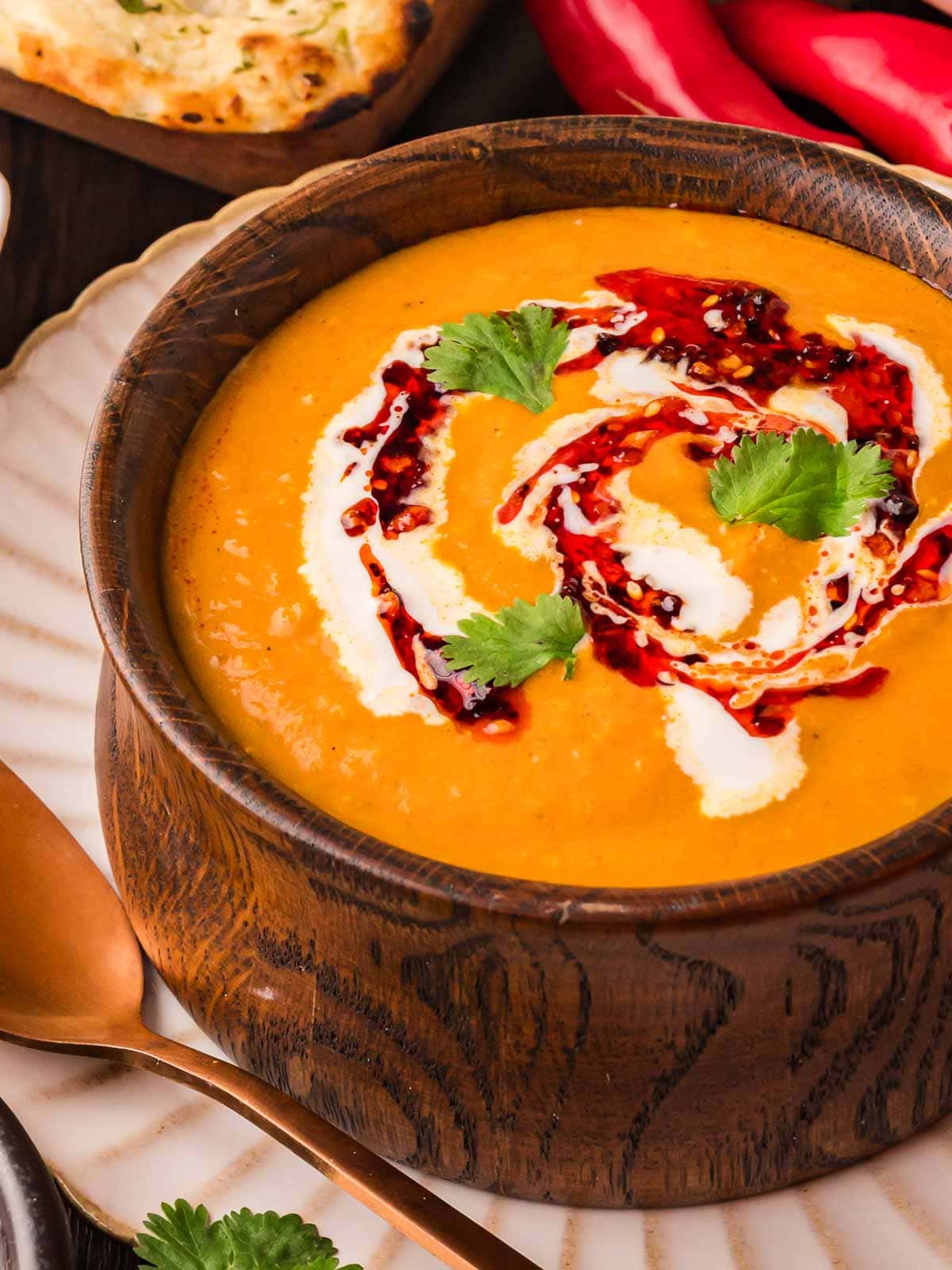 Pumpkin coconut curry soup served in a rustic wooden bowl with cream and chili oil garnish, ready to eat.