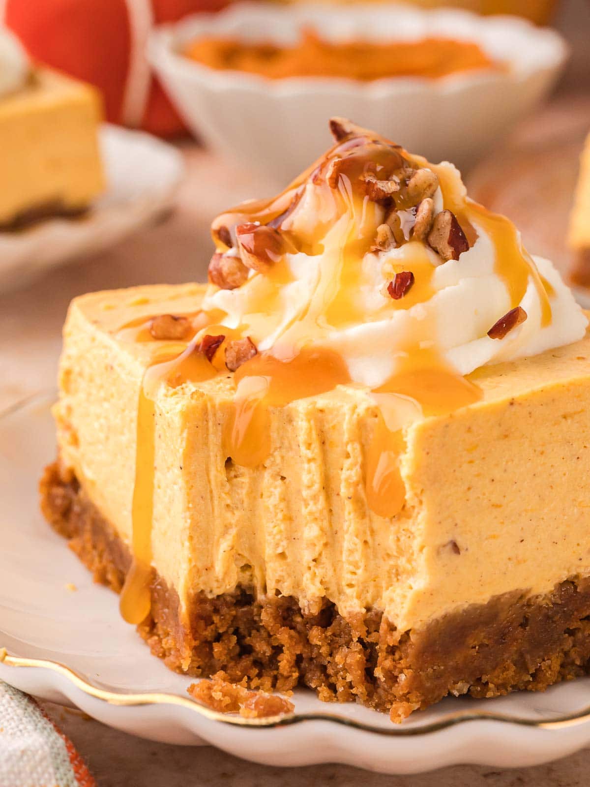 Close-up of no-bake pumpkin cheesecake bar with a bite missing, showing creamy pumpkin filling, whipped cream, pecans, and caramel sauce.