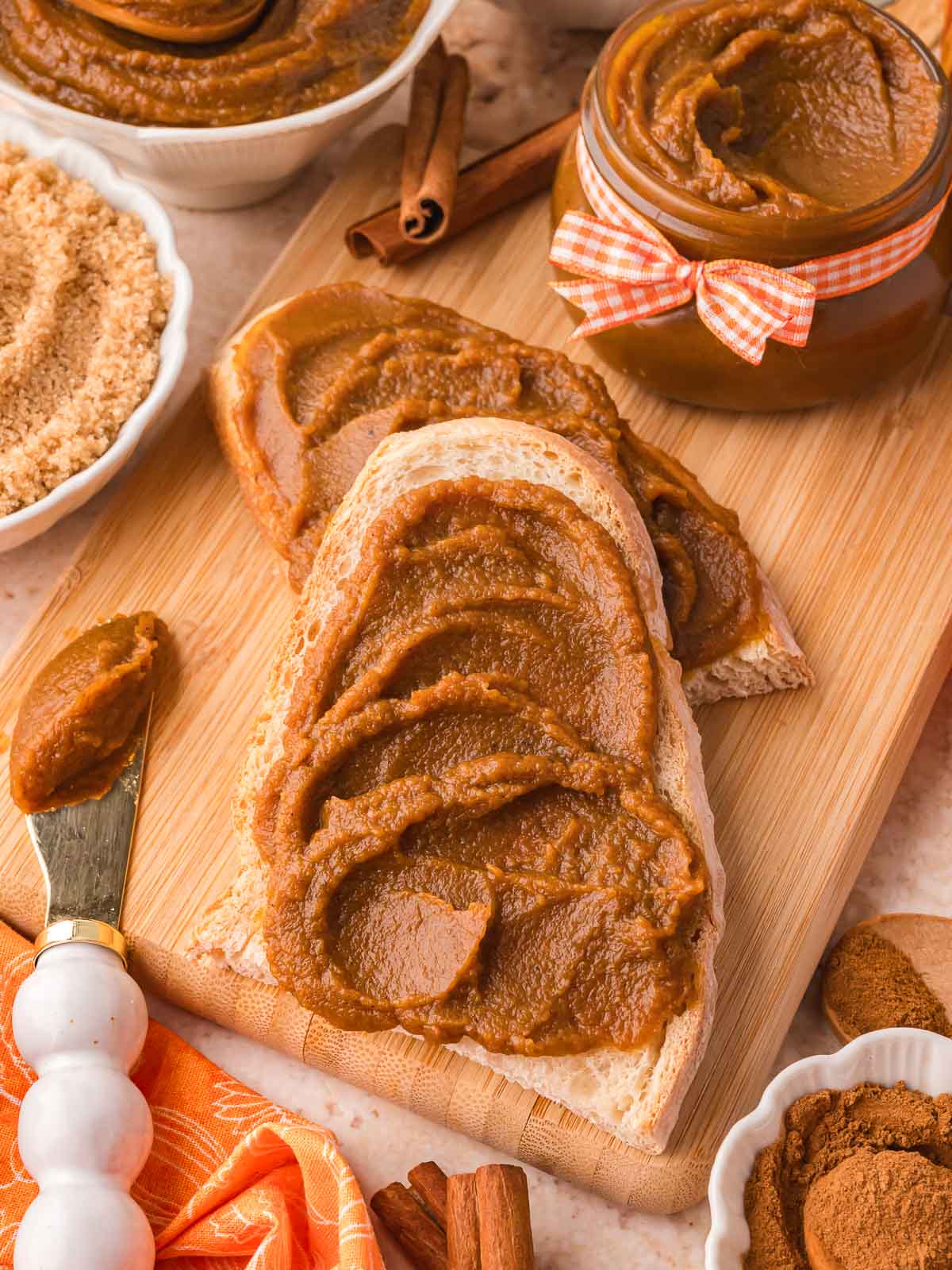 Thick slices of rustic bread generously spread with pumpkin butter on a wooden cutting board, styled with cinnamon sticks and a jar of pumpkin butter.
