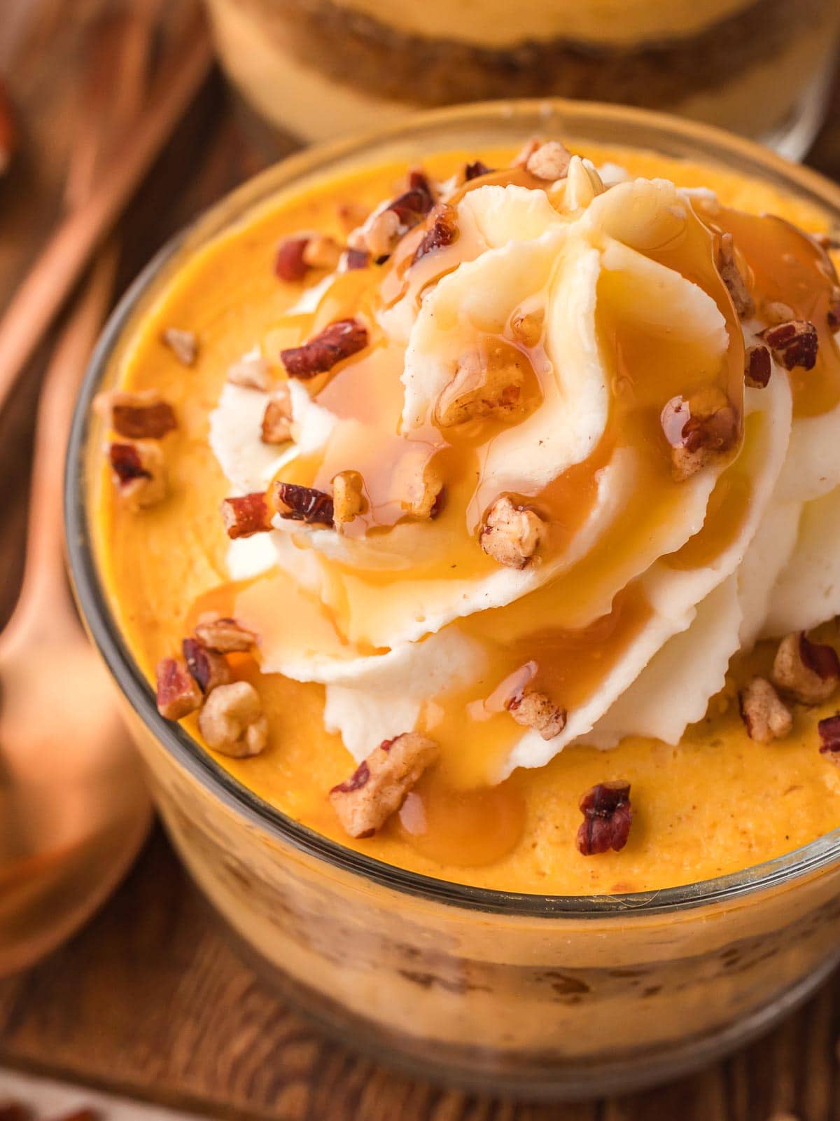 Close-up of pumpkin pie cheesecake cup topped with whipped cream, chopped pecans, and caramel drizzle.