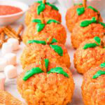 Front view of multiple Rice Krispie Pumpkins on a table with decorating ingredients in the background.