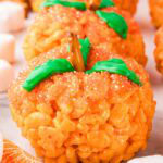 Close-up of Rice Krispie Pumpkins showing pretzel stalks and green icing leaves on top of orange sanding sugar coating.