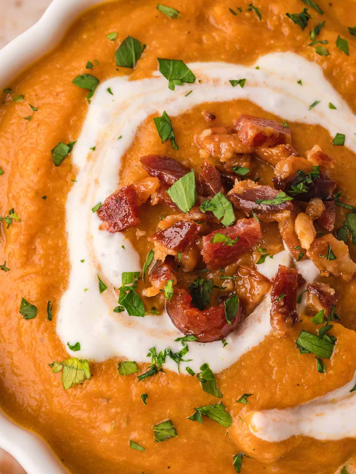 Close-up of slow cooker pumpkin soup with crispy bacon crumbles, parsley, and a swirl of cream.