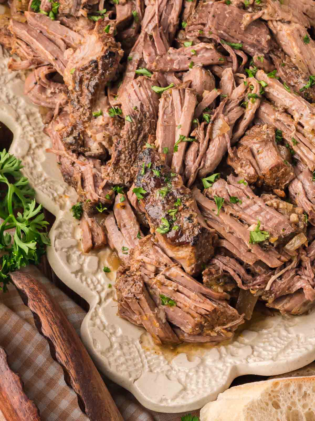 Tender shredded beef on a platter garnished with parsley, ready to serve with bread and sides.