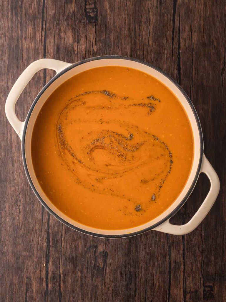 Blended pumpkin coconut curry soup in a Dutch oven, with swirls of soy sauce and black pepper on top.