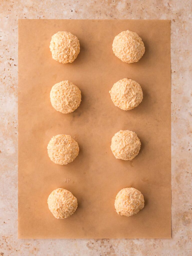 Eight shaped mini cheese balls on parchment paper, ready for coating and decorating into pumpkin-shaped appetizers.