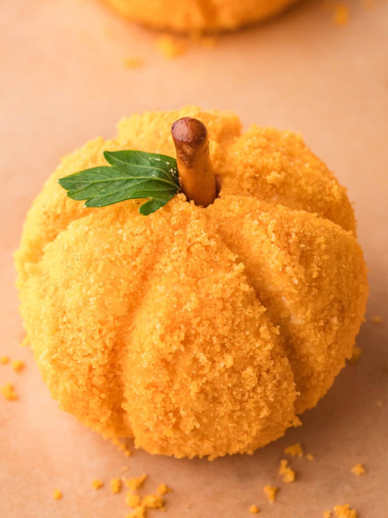 Finished mini pumpkin cheese ball topped with a pretzel stick stem and parsley leaf, coated in crushed cheese crackers.