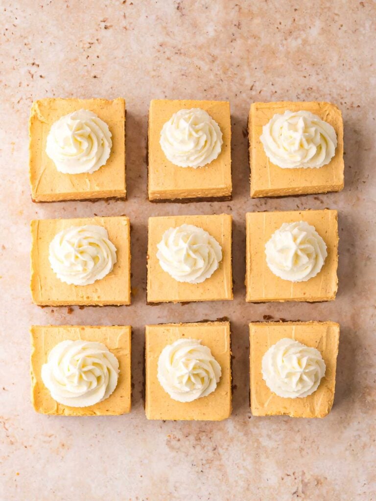 Nine no-bake pumpkin cheesecake bars cut into squares, each topped with whipped cream swirls.