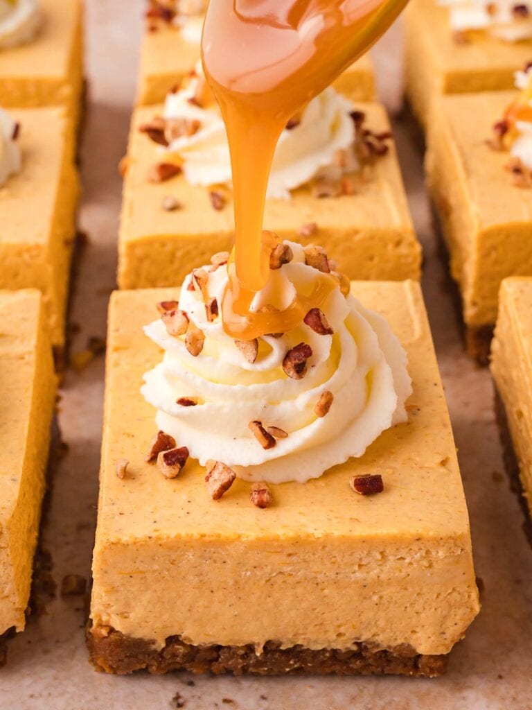 Close-up of no-bake pumpkin cheesecake bar topped with whipped cream, pecans, and caramel drizzle.