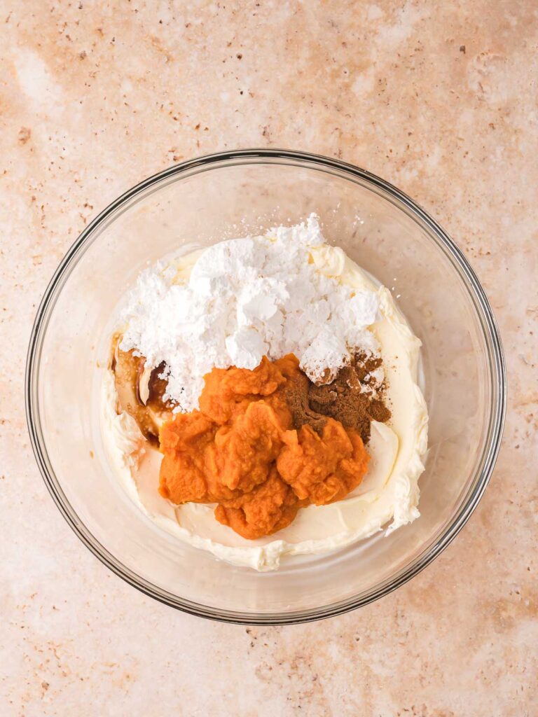 Cream cheese mixture with pumpkin purée, powdered sugar, and spices in a glass bowl for no-bake pumpkin cheesecake bars.