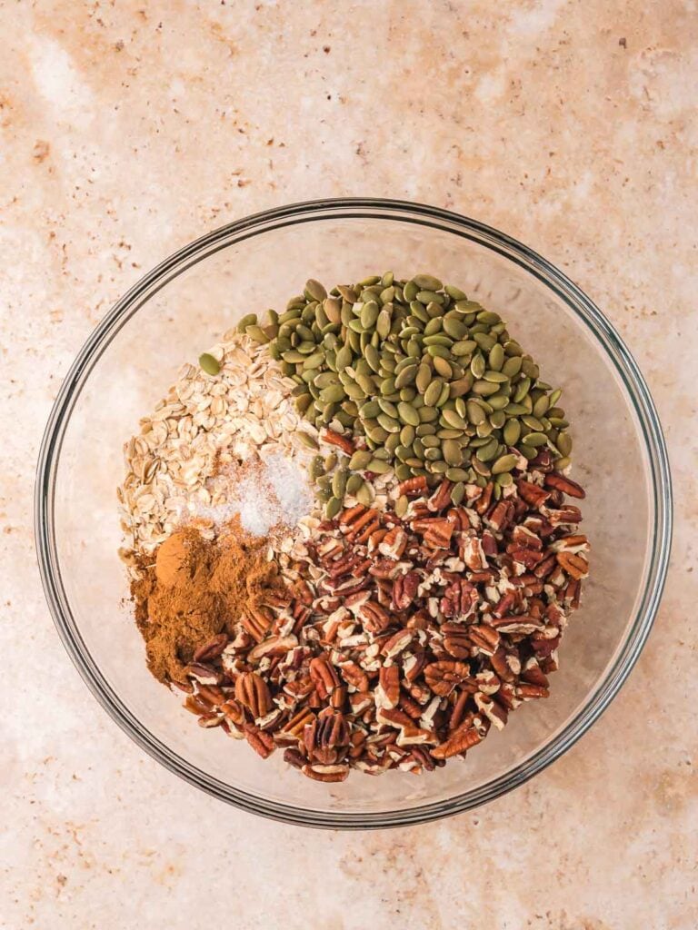 Bowl of oats, pecans, pumpkin seeds, and spices for pumpkin granola.