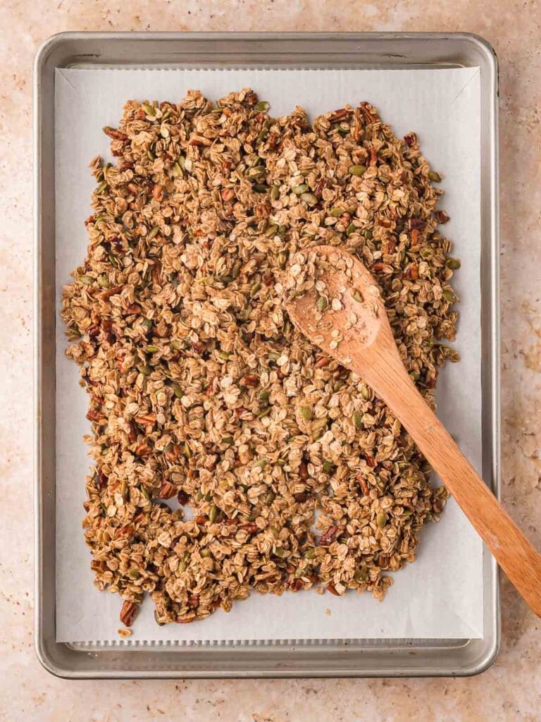 Pumpkin granola spread on a parchment-lined baking sheet before baking.