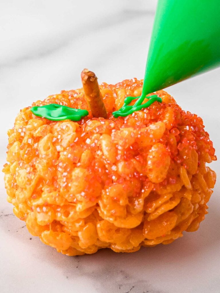 Piping green icing leaves onto a Rice Krispie Pumpkin with a pretzel stalk.
