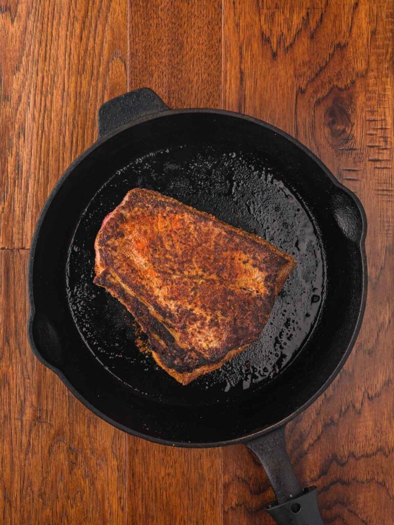 Chuck roast searing in a cast iron skillet to build flavor before slow cooking.
