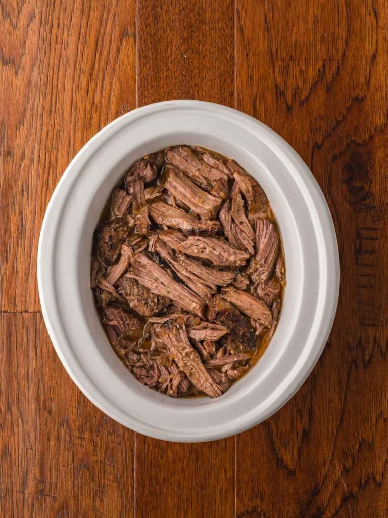 Juicy shredded beef mixed into flavorful cooking juices in a slow cooker.