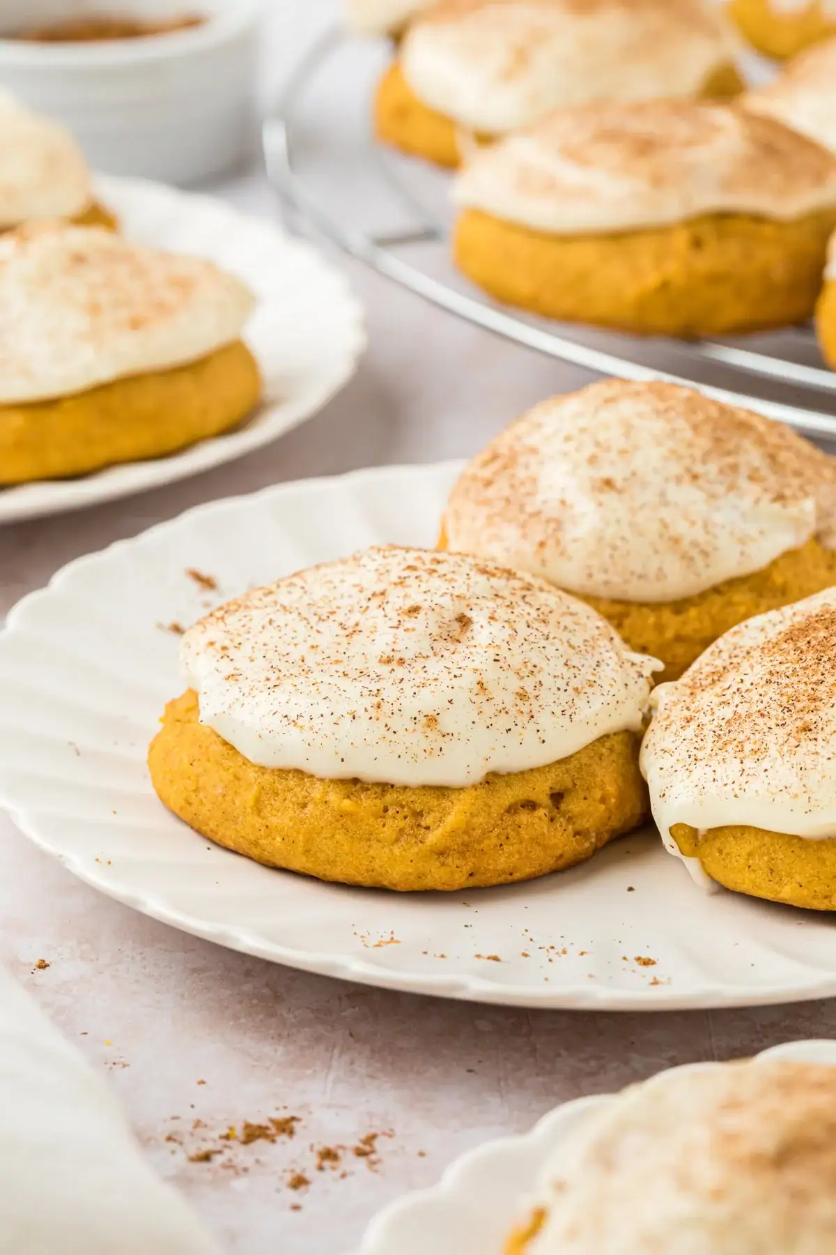 Soft pumpkin spice cookies topped with fluffy cream cheese frosting and dusted with cinnamon, displayed on a white plate.