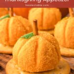 Close-up of a mini pumpkin cheese ball with a pretzel stem and parsley leaf on a round cracker by Tessie's Table.