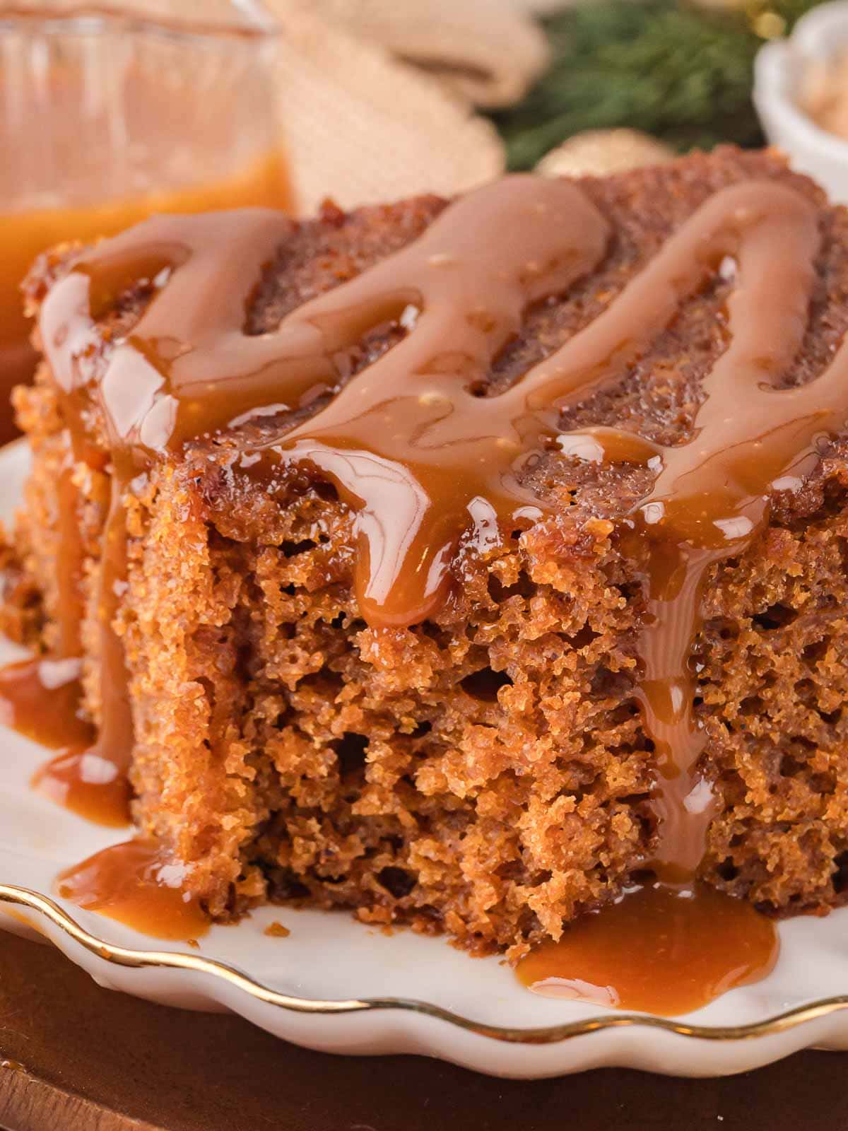 Close-up of a slice of Gingerbread Cake topped with thick caramel sauce on a white plate.