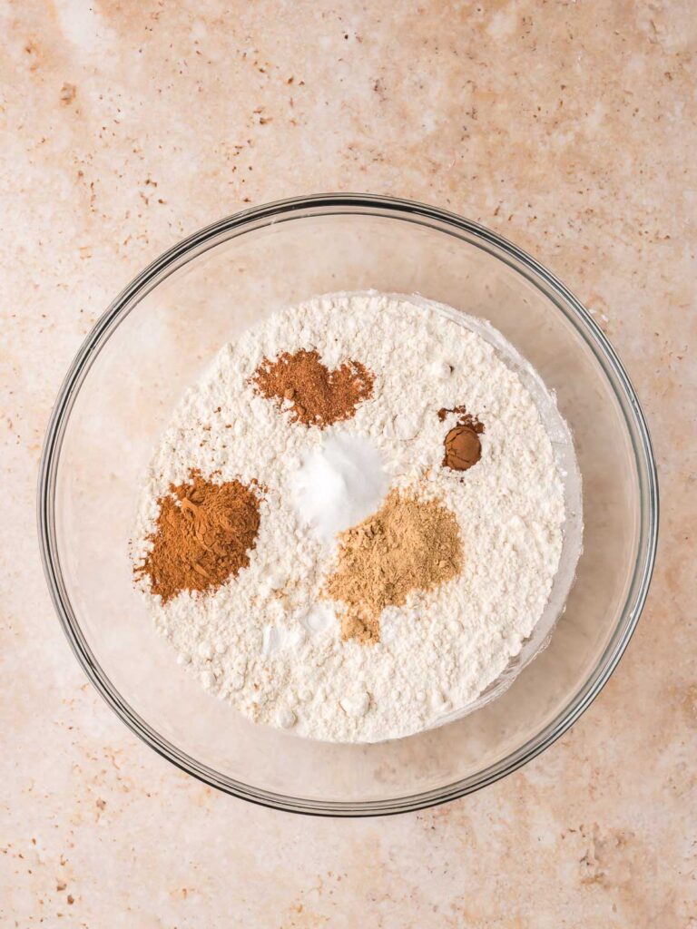 Bowl of flour, baking soda, and warm spices for Gingerbread Cake on a light countertop.