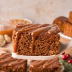 Slice of Gingerbread Cake drizzled with caramel sauce held on a spatula above more cake squares.