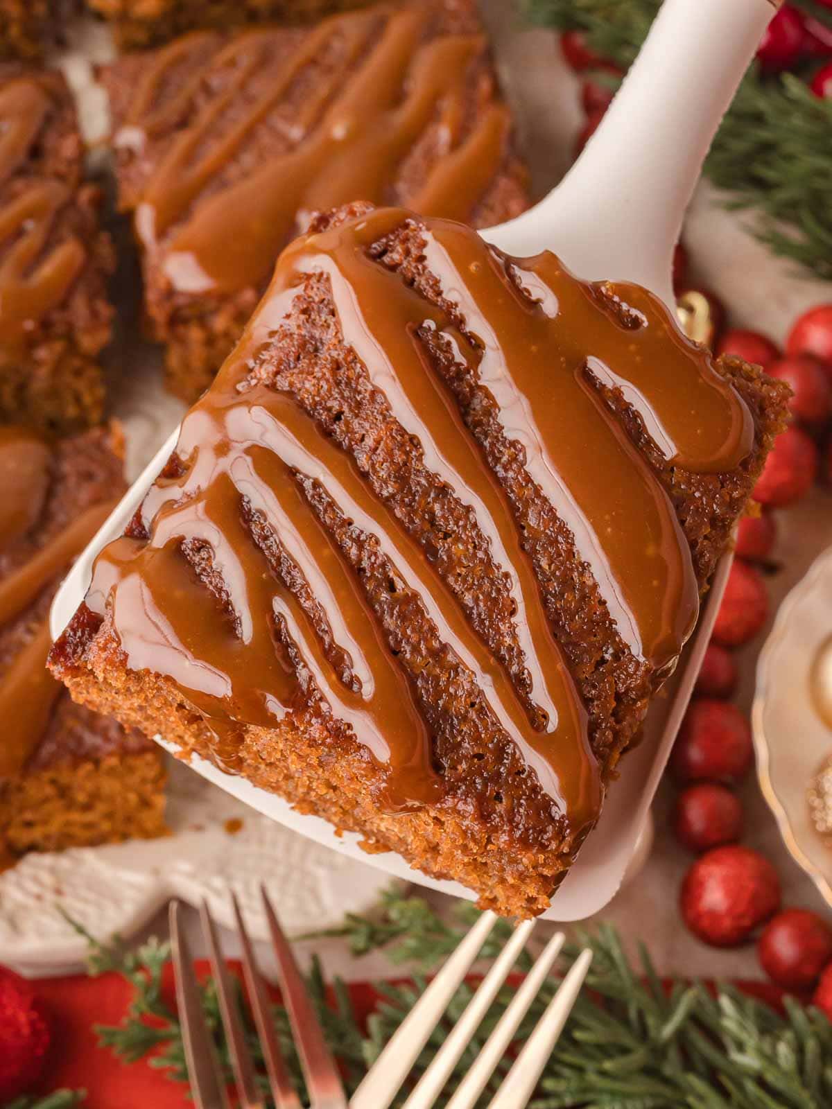 Overhead view of a single slice of Gingerbread Cake on a spatula with caramel sauce drizzled on top.