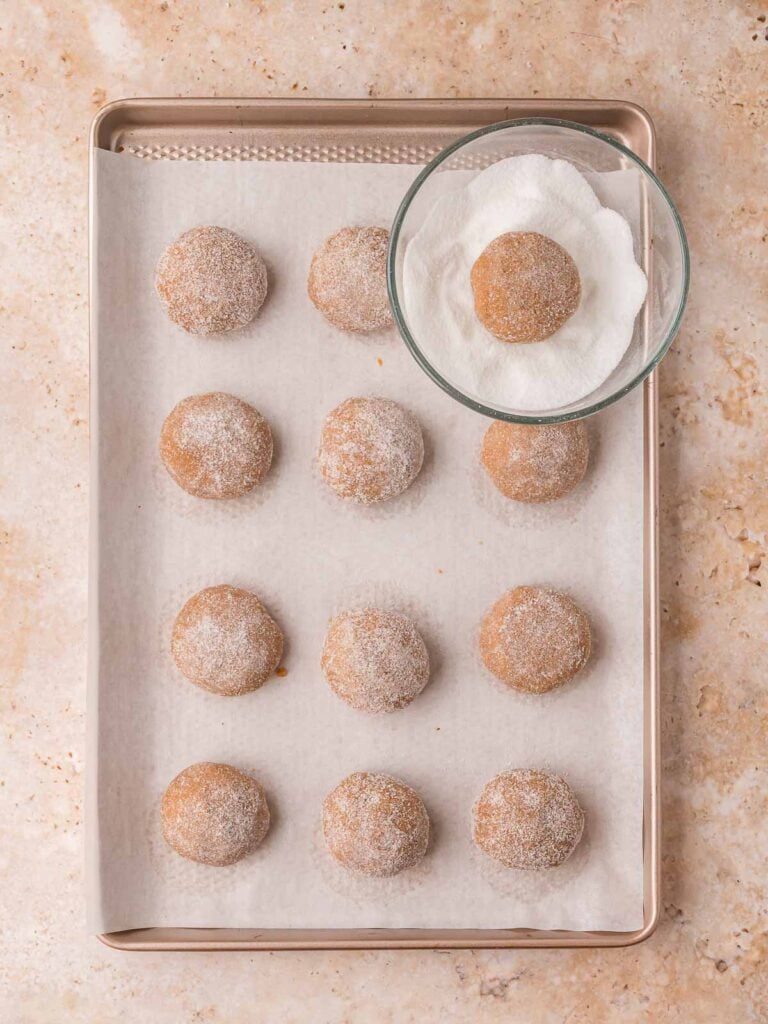 Gingerbread cookie dough balls rolled in sugar and arranged on a parchment-lined baking tray before baking.
