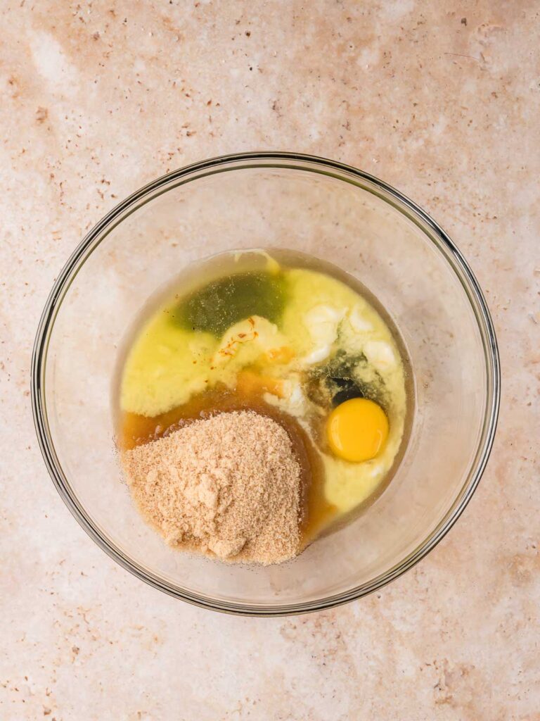 Melted butter, brown sugar, molasses, and egg in a glass bowl to make the spiced gingerbread cookie dough.