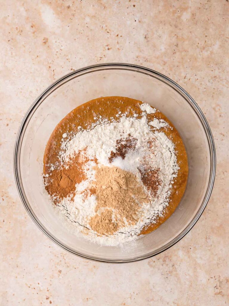 Flour and warm spices including ginger, cinnamon, nutmeg, and cloves added to the gingerbread cookie dough mixture.