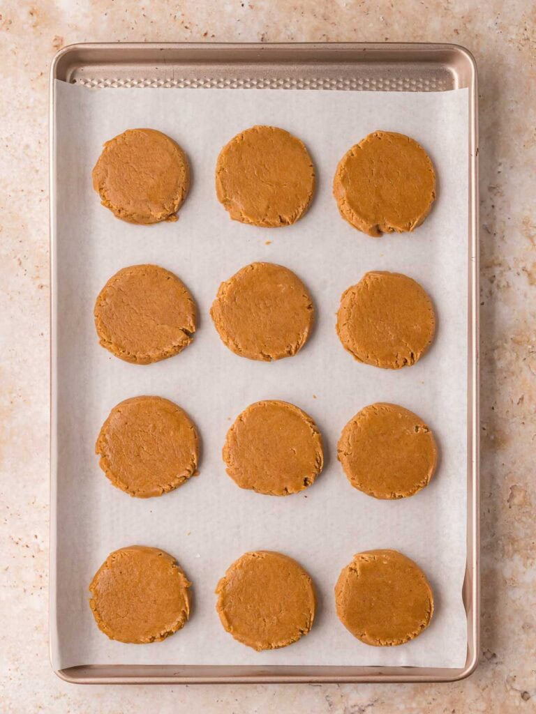 Flattened portions of gingerbread dough arranged on a parchment-lined baking sheet ready for filling.