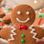 Close-up of a smiling Gingerbread Man Cookie with red bow tie and green buttons, surrounded by festive holiday treats.