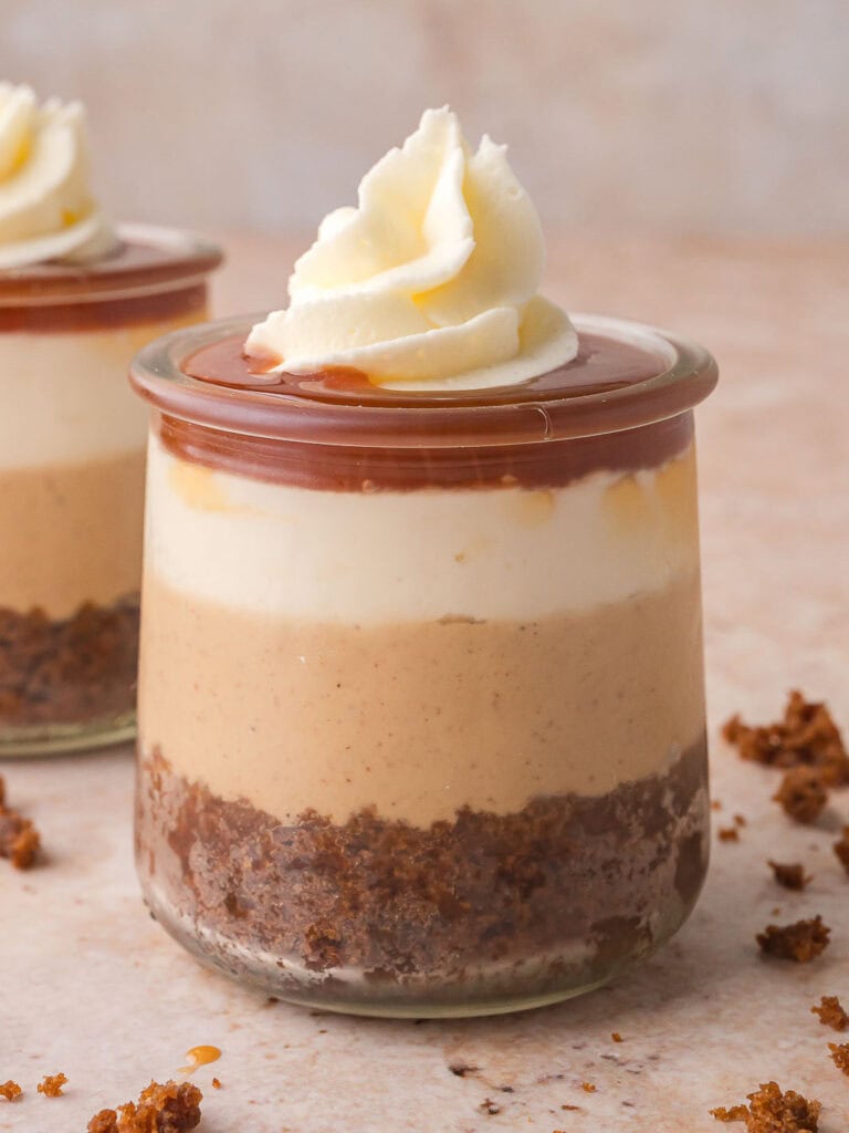 Finished trifle topped with a swirl of whipped cream and a drizzle of caramel, showing the layered gingerbread and cheesecake inside the glass.
