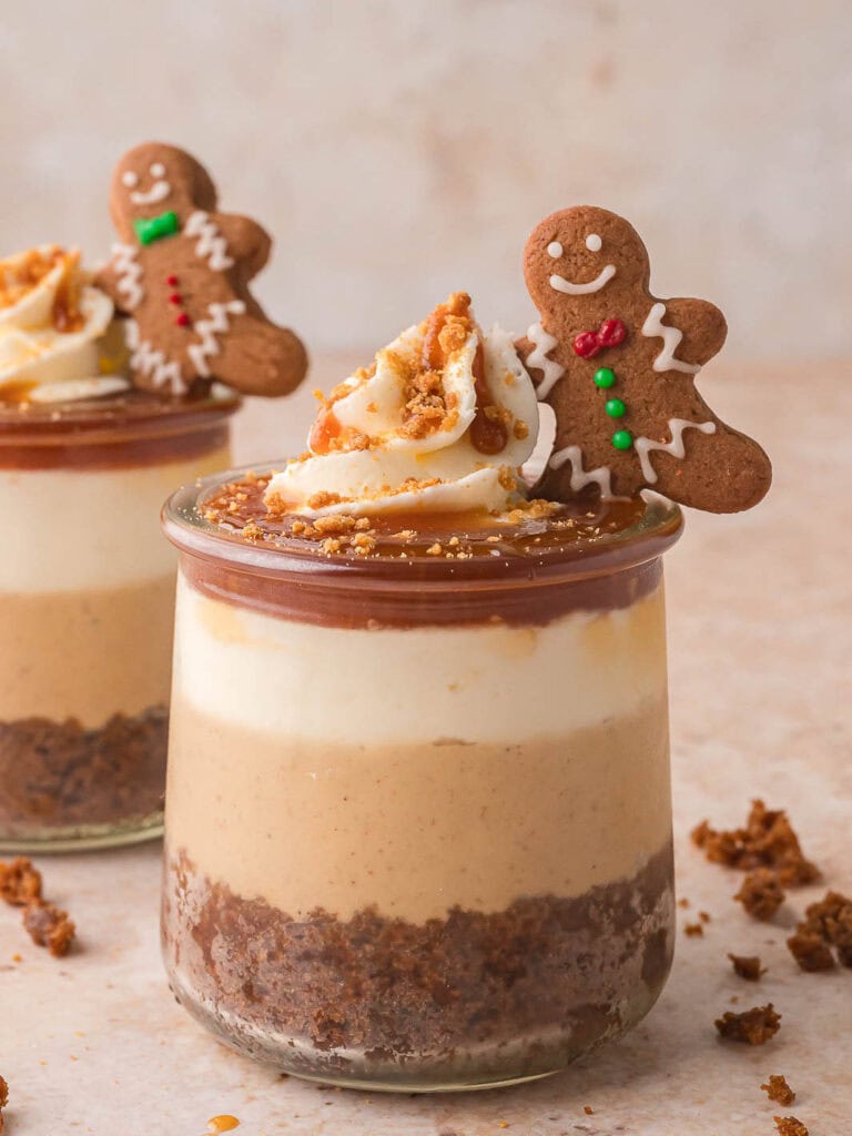 Fully decorated Mini Gingerbread Trifles topped with whipped cream, crushed cookies, caramel drizzle, and a mini gingerbread man cookie for garnish.