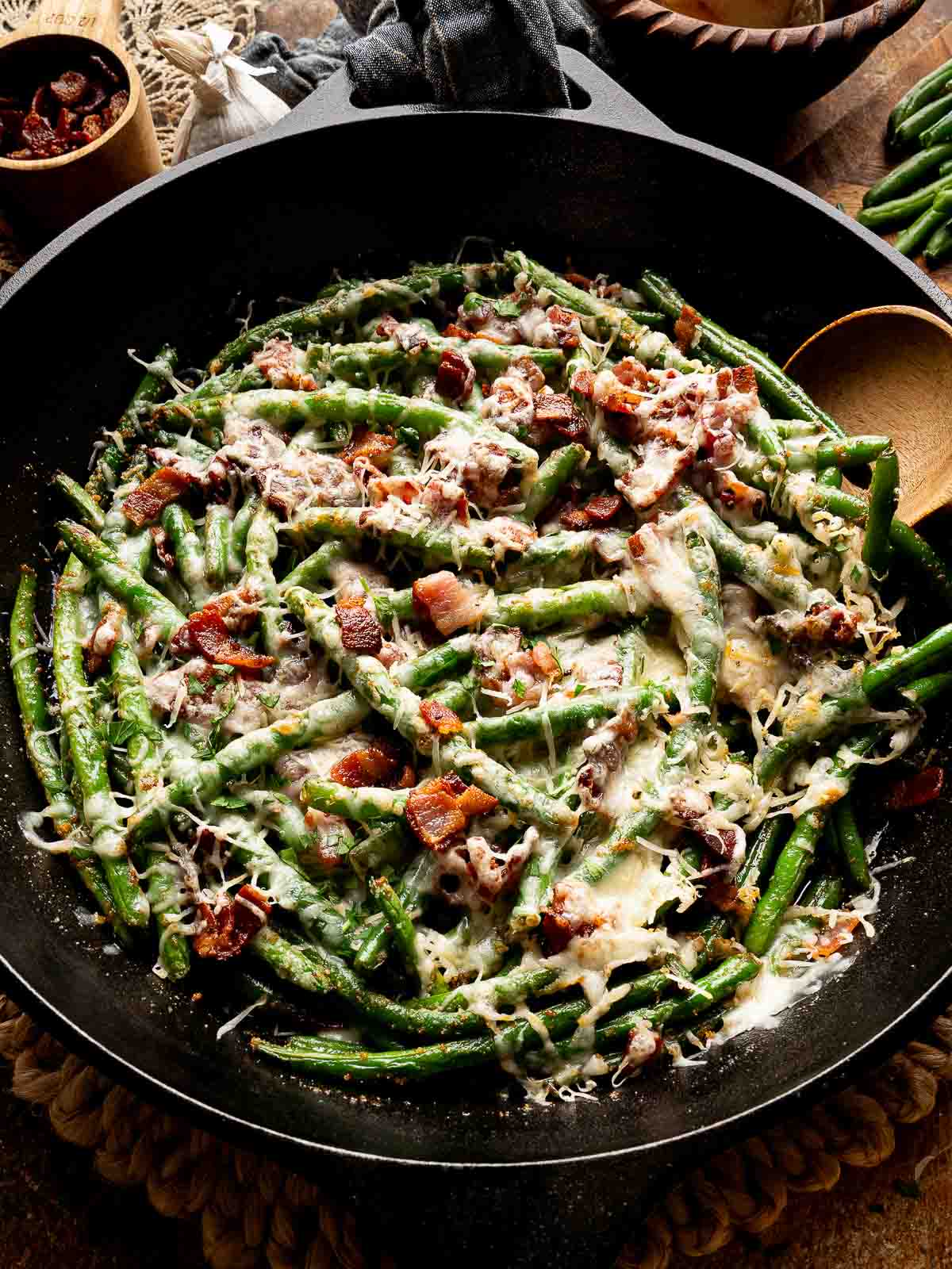 Overhead shot of cheesy bacon green beans in cast iron skillet with serving spoon.