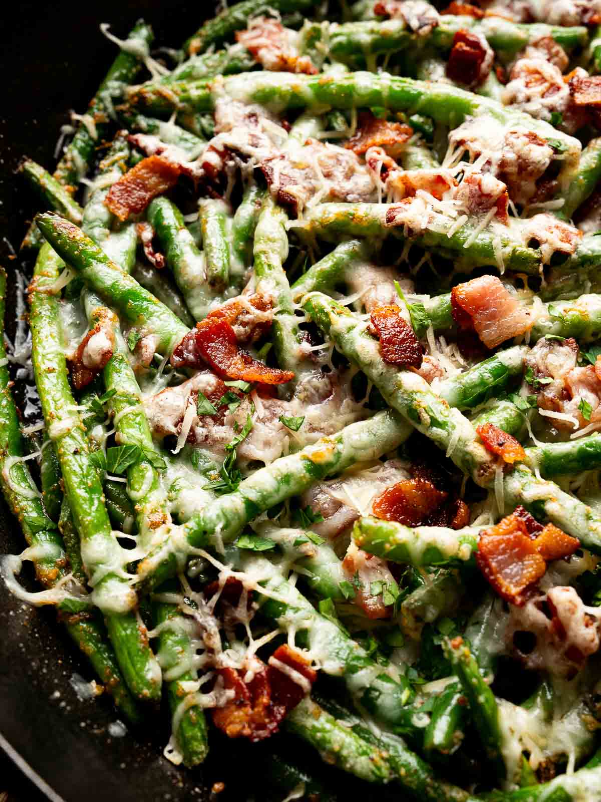 Close-up of cheesy green beans with bacon and Parmesan served on a black plate.