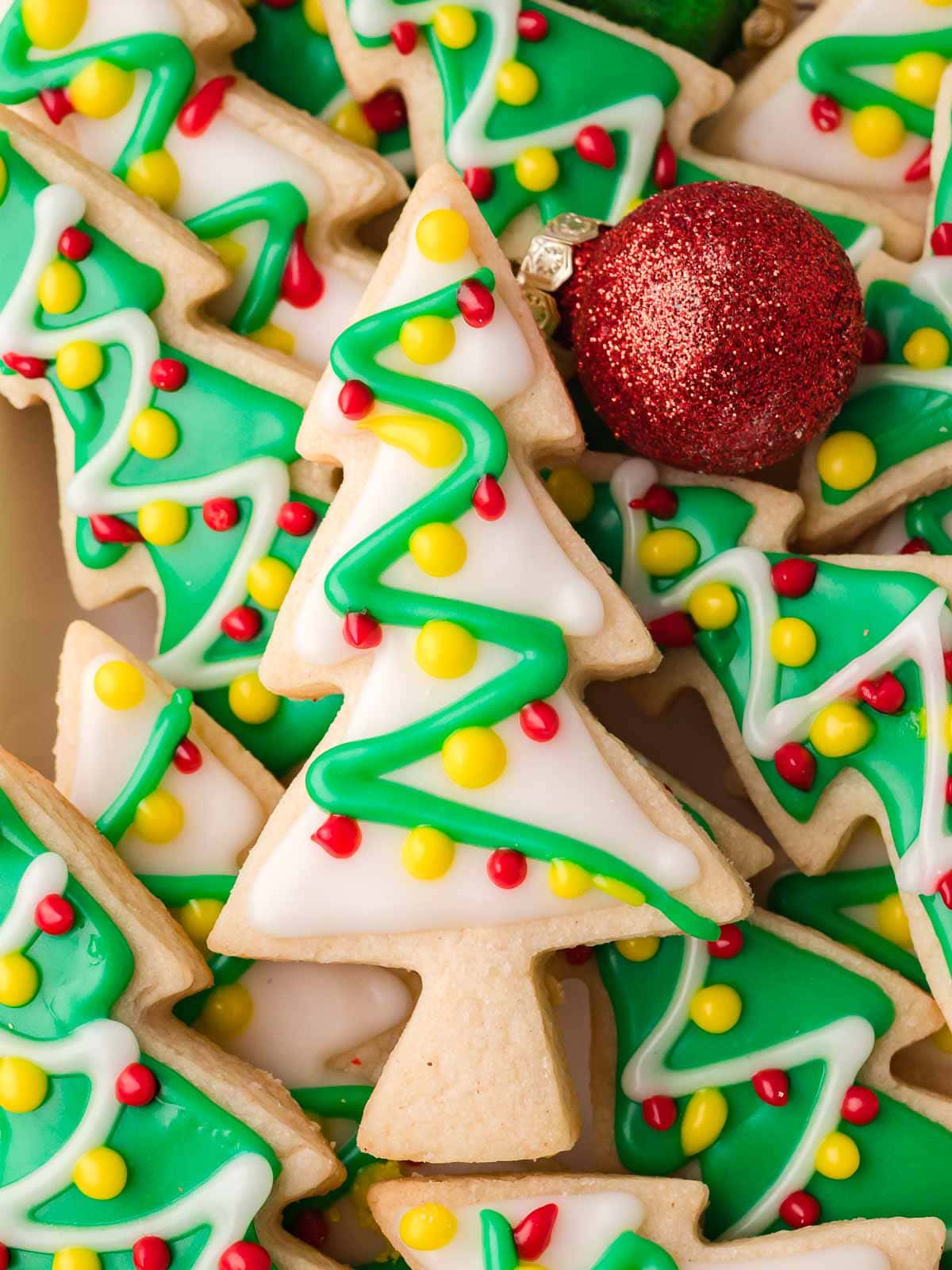 Close-up of decorated Christmas tree sugar cookies with shiny glaze and a red glitter ornament.