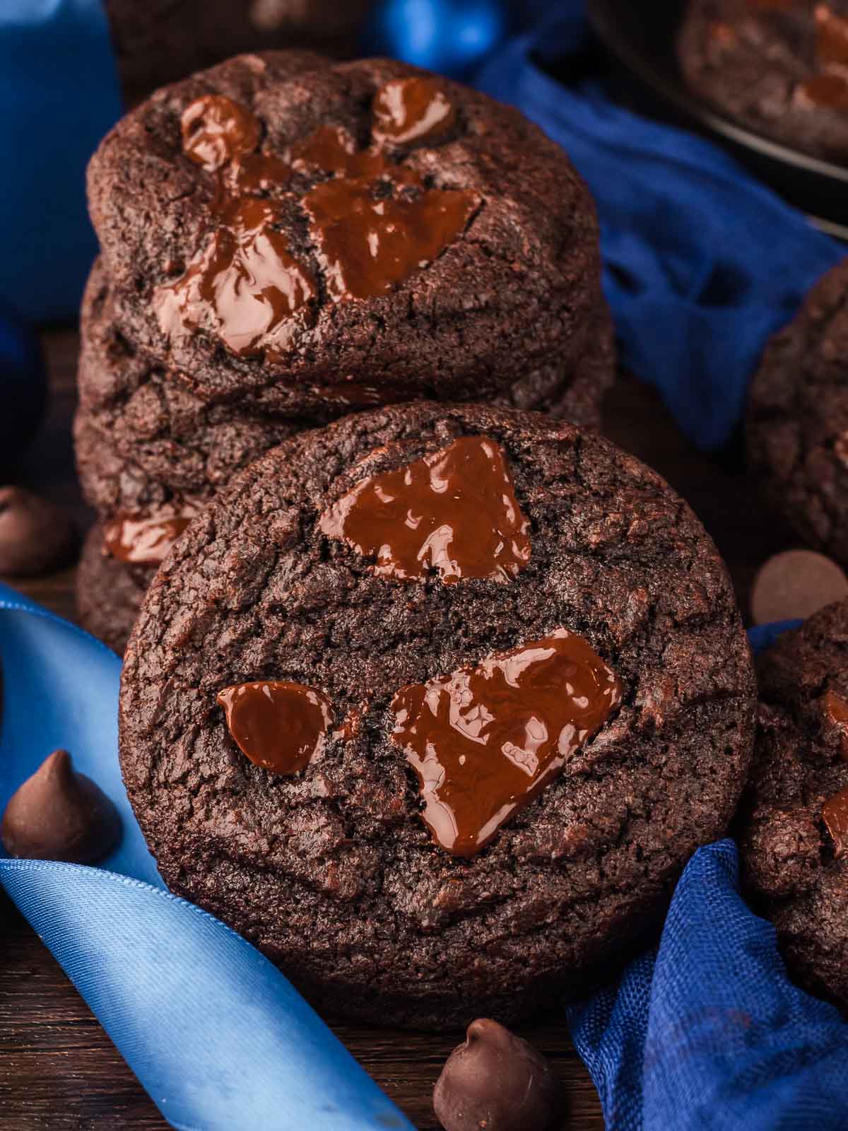 Stack of thick Double Chocolate Chunk Cookies with melted chocolate and dark chocolate bars nearby.