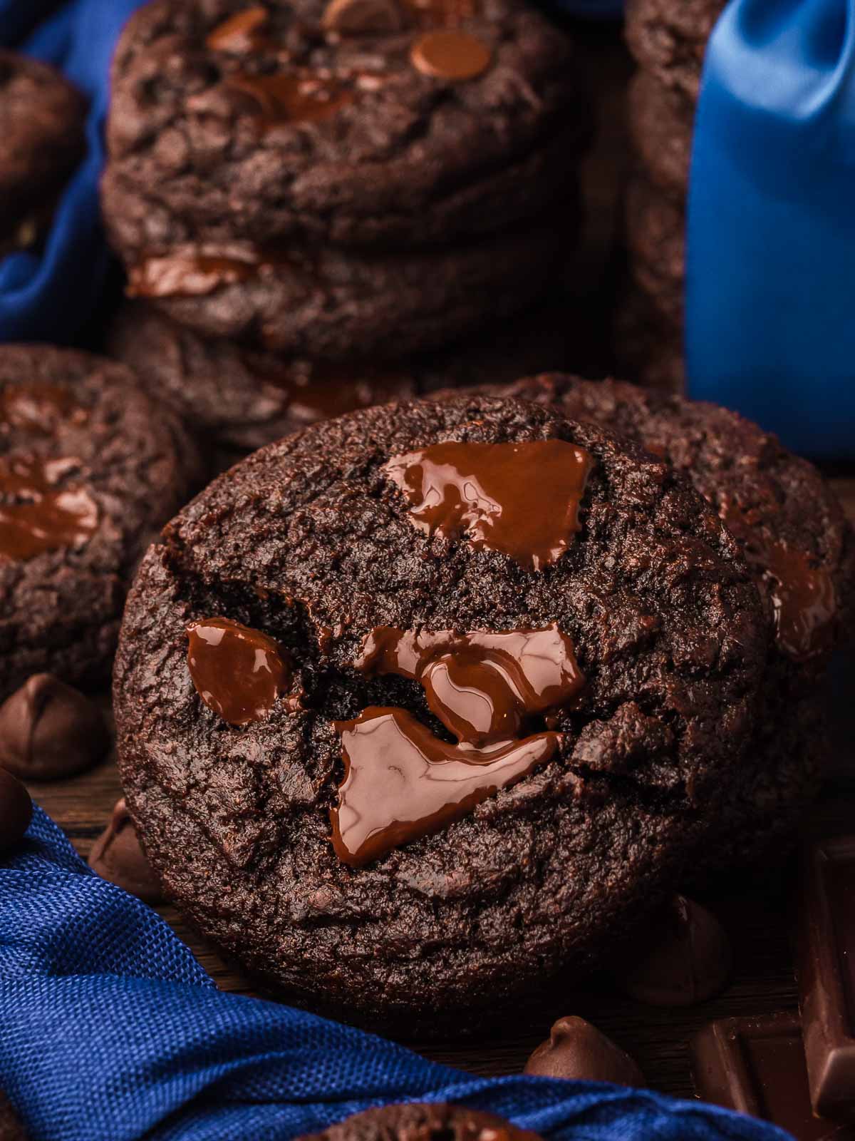 Stack of Double Chocolate Chunk Cookies with melted chocolate centers, surrounded by chocolate pieces and blue ribbon.