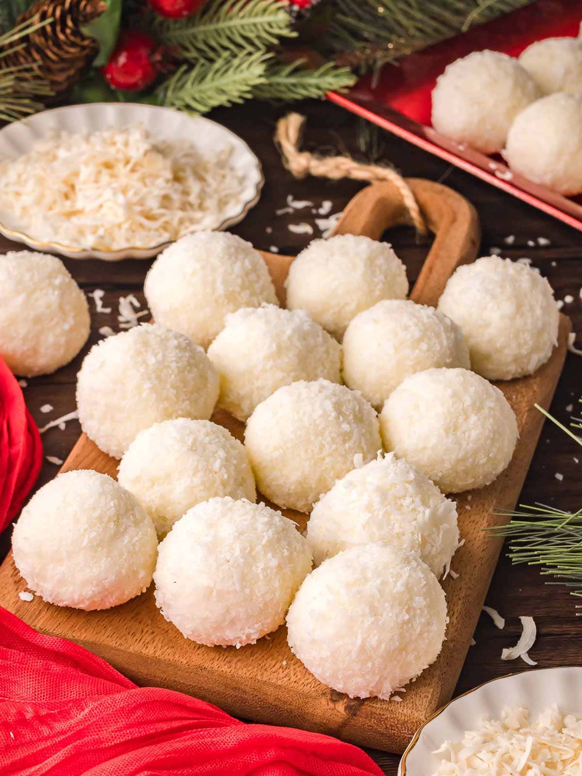 No-bake Coconut Snowball Cookies arranged on a wooden board surrounded by holiday decor and shredded coconut.