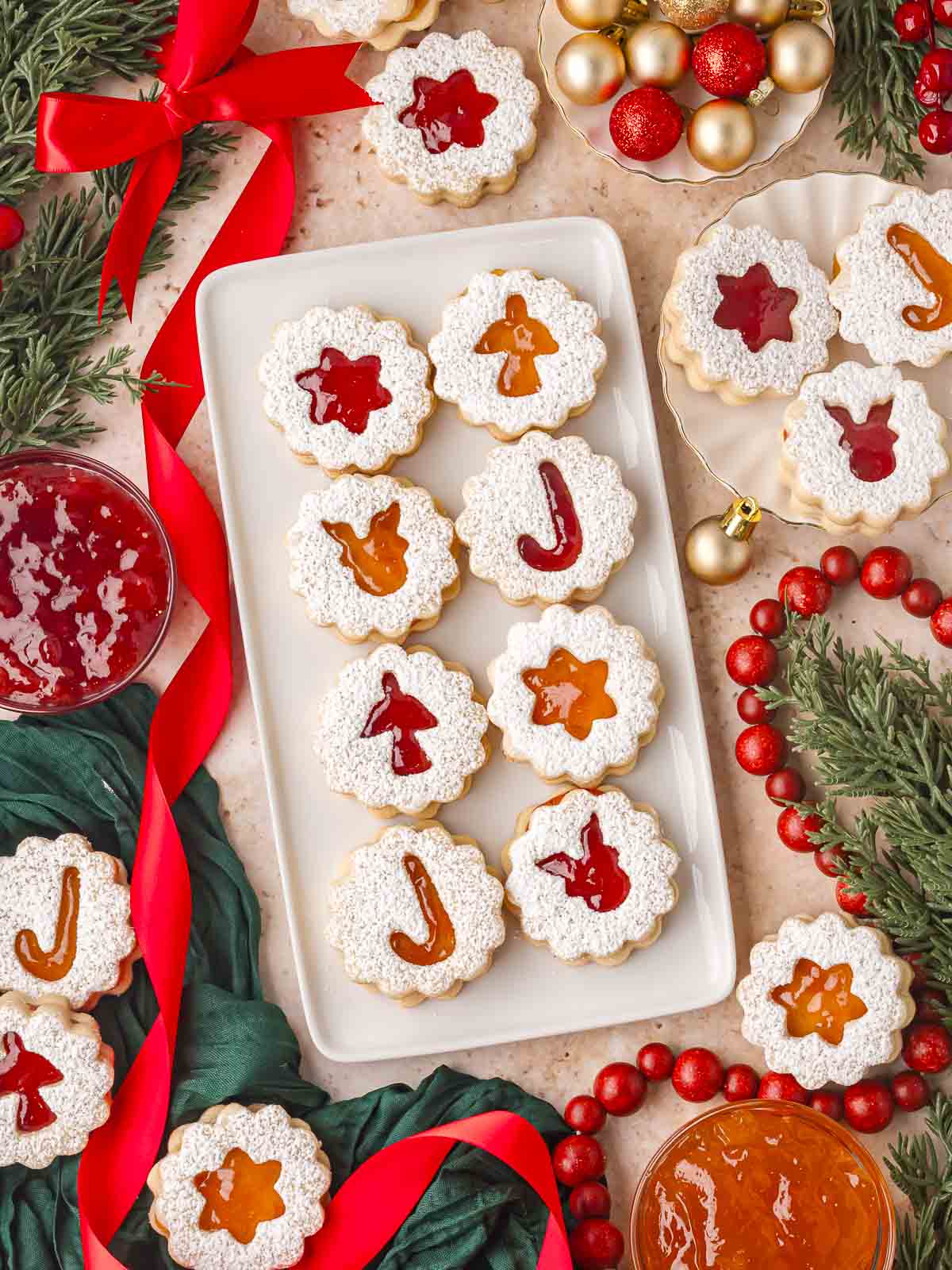 Festive Linzer cookies on a white plate with powdered sugar, red ribbons, and ornaments.