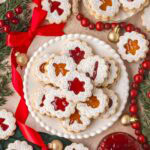 Jam-filled Linzer cookies arranged with red bows, cranberries, and gold ornaments for a Christmas spread.