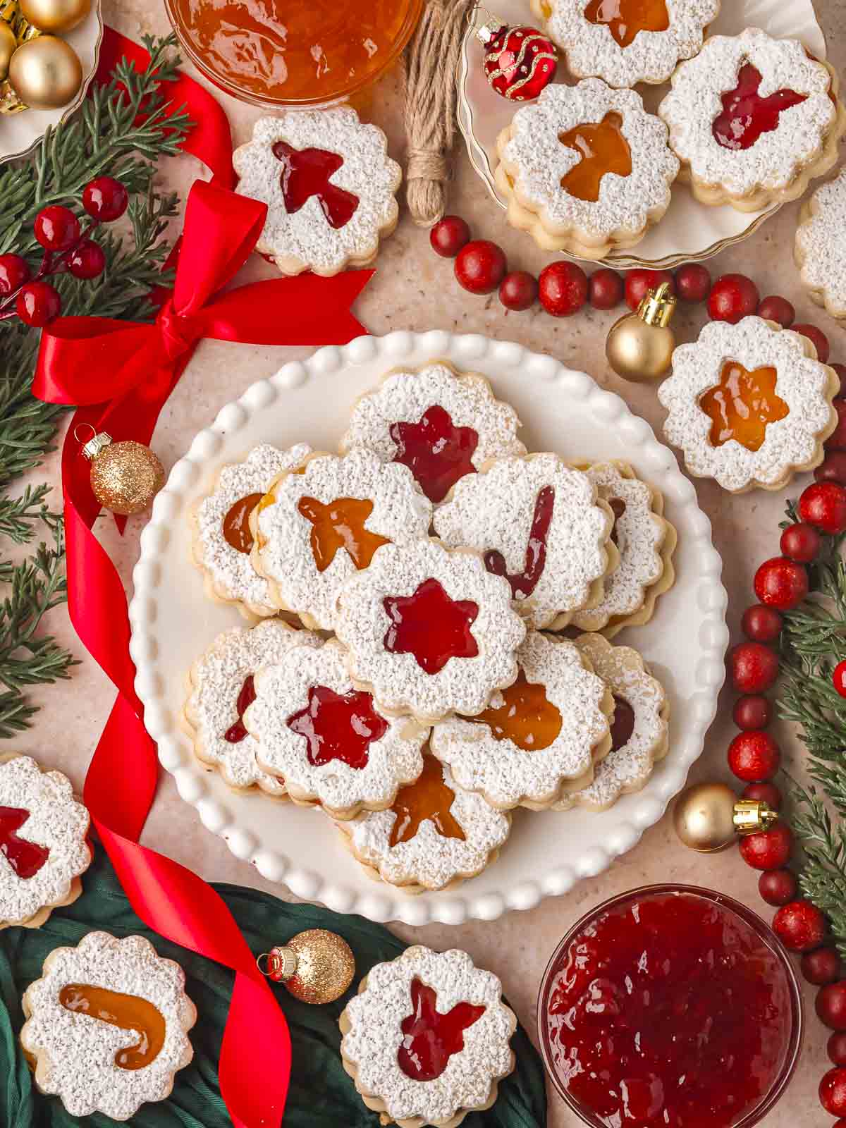 Jam-filled Linzer cookies arranged with red bows, cranberries, and gold ornaments for a Christmas spread.