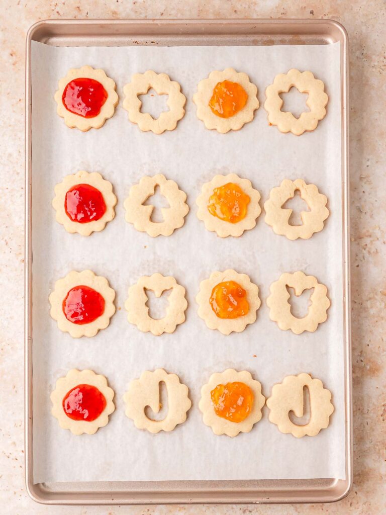 Baked cookie bottoms spread with raspberry and apricot jam before sandwiching.