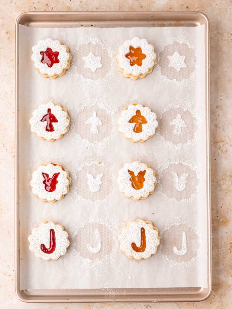 Assembled Linzer cookies filled with jam and dusted with sugar on a baking tray.