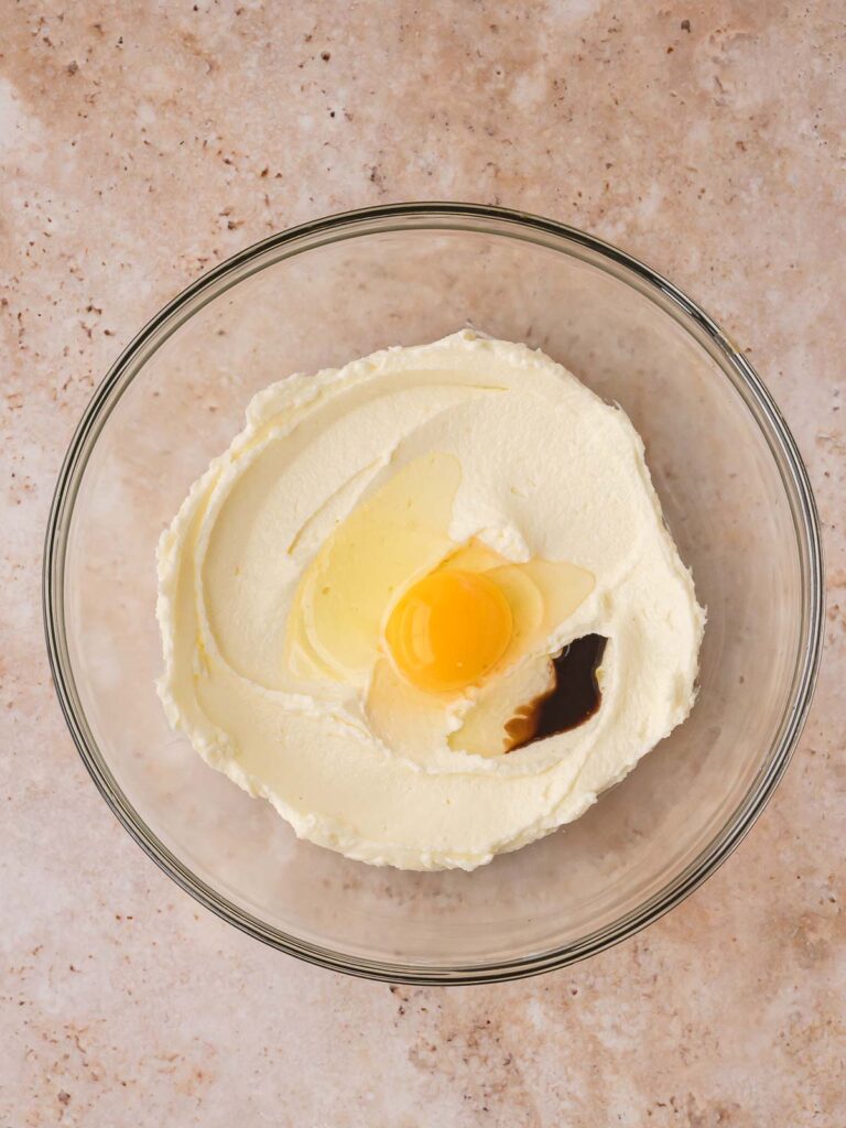 Egg and vanilla extract being mixed into the creamed butter and sugar.
