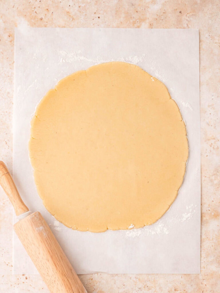 Chilled Linzer cookie dough rolled out evenly on parchment paper with a rolling pin.